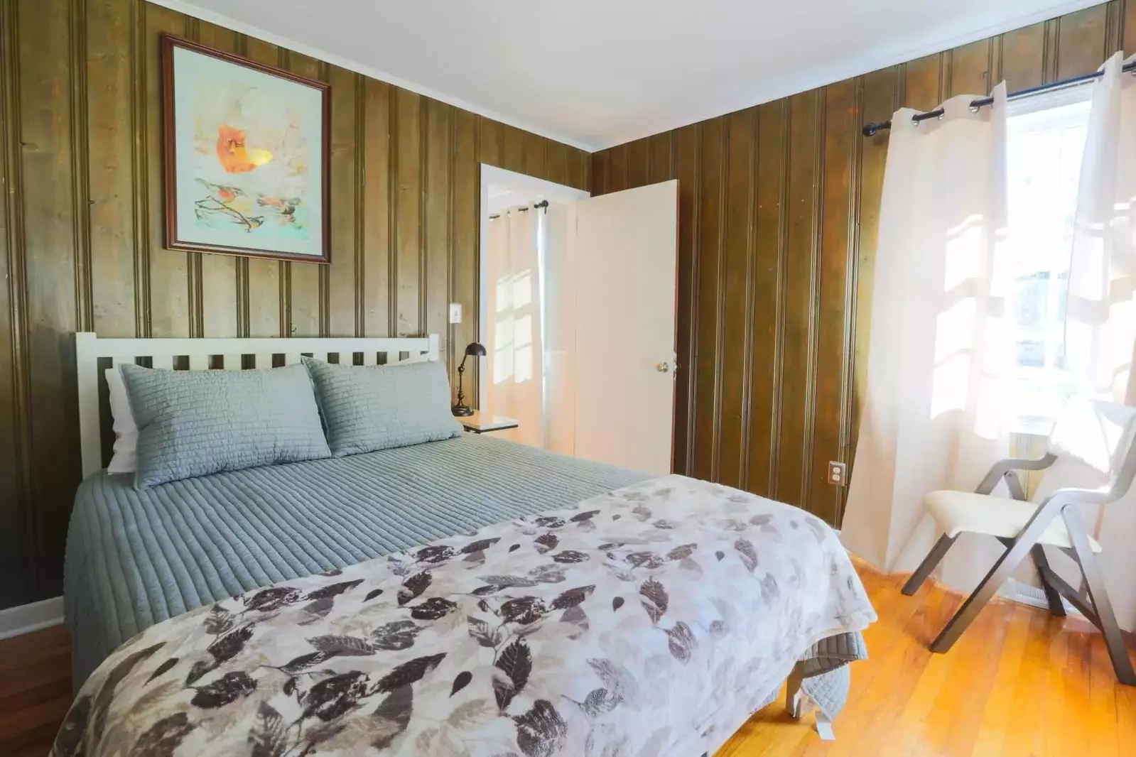 This bedroom features a queen size bed, hardwood floors and a nightstand with a reading lamp.