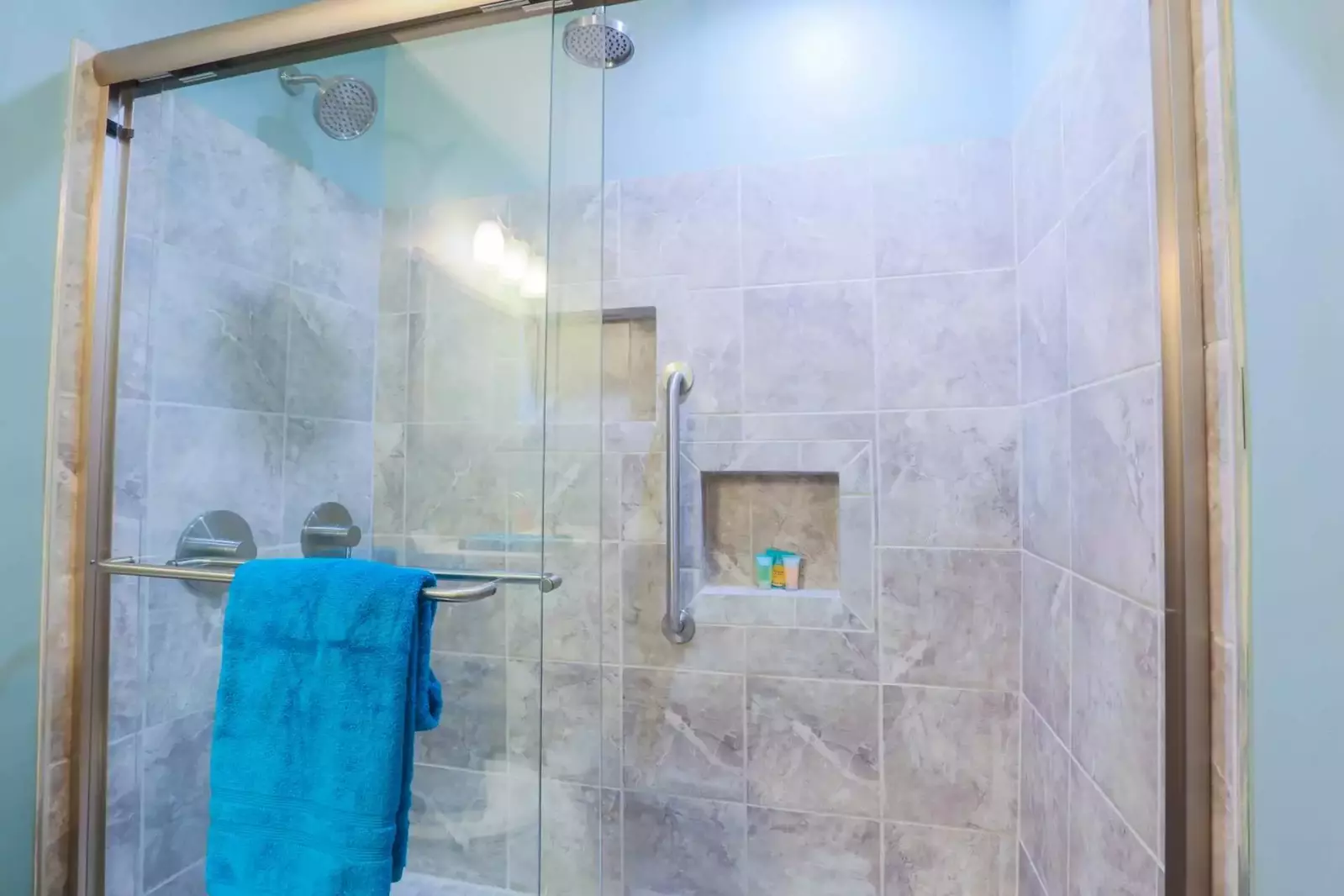 The tiled shower also has two rain showerheads and sliding glass doors.