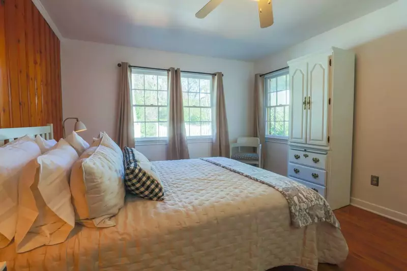 This bedroom features a queen size bed, armoire, ceiling fan and reading lamps.