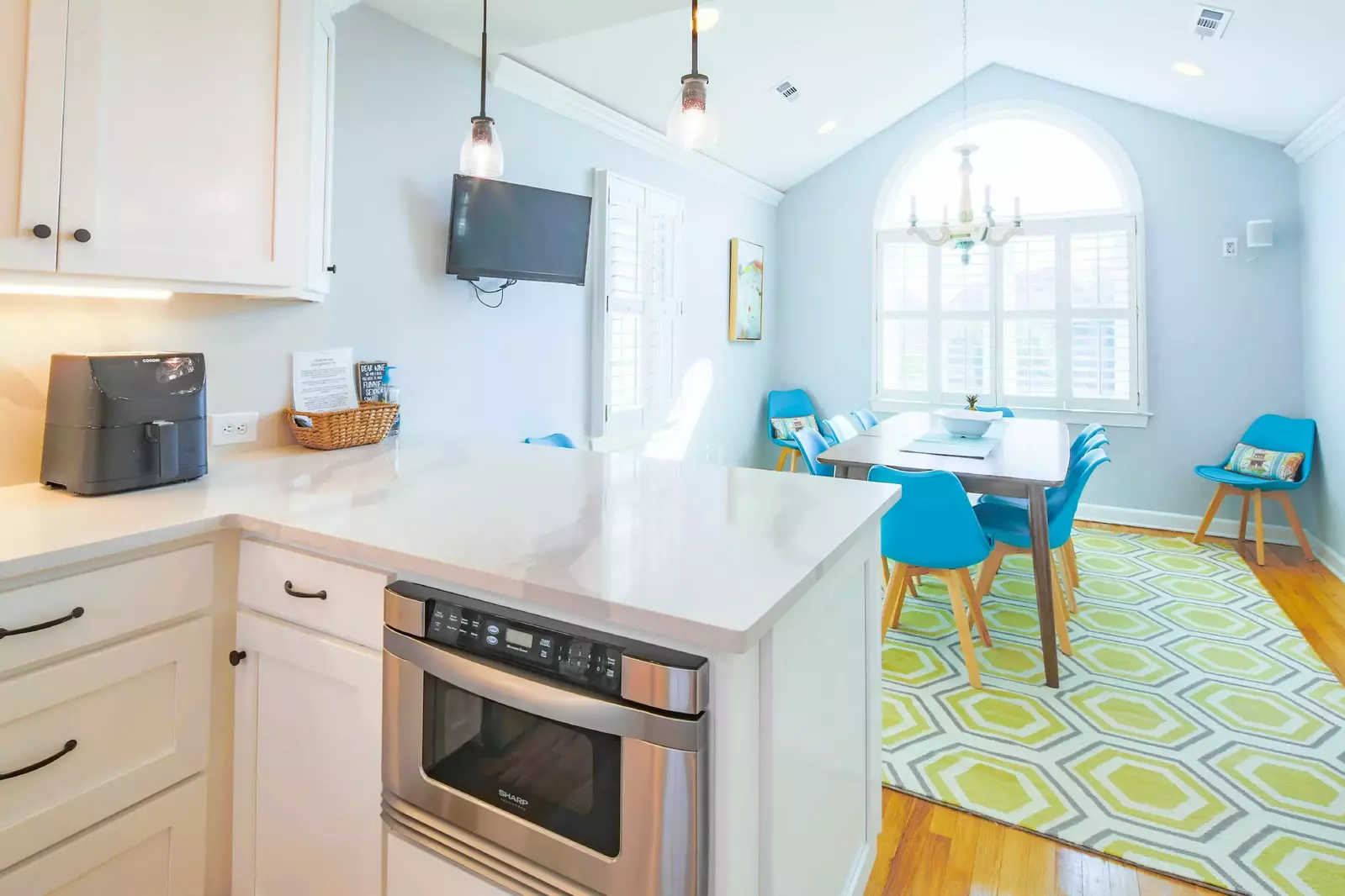 The kitchen opens into the dining room with a wall-mounted TV and lovely natural light.