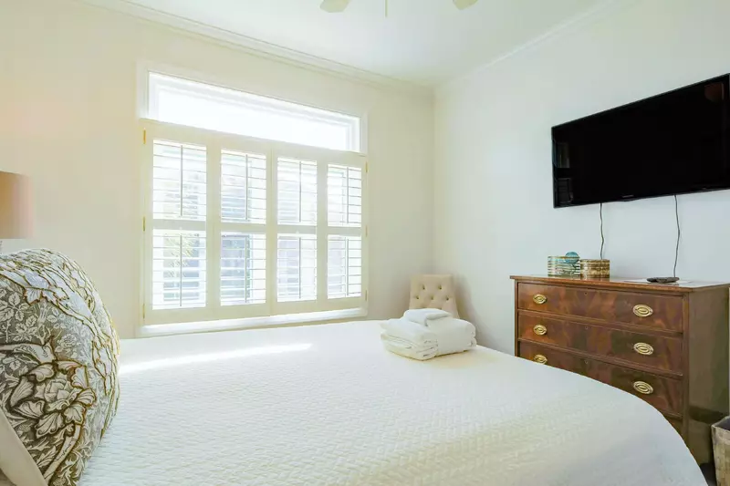 This guest bedroom features a dresser, wall-mounted smart TV and lovely natural light.