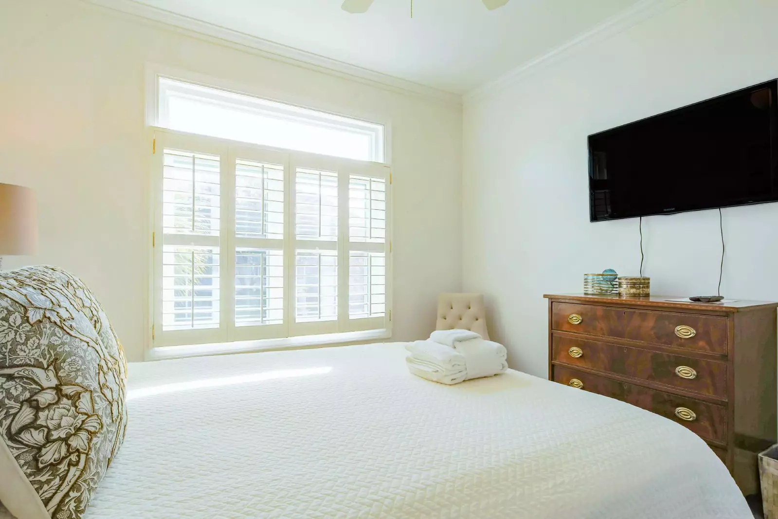 This guest bedroom features a dresser, wall-mounted smart TV and lovely natural light.