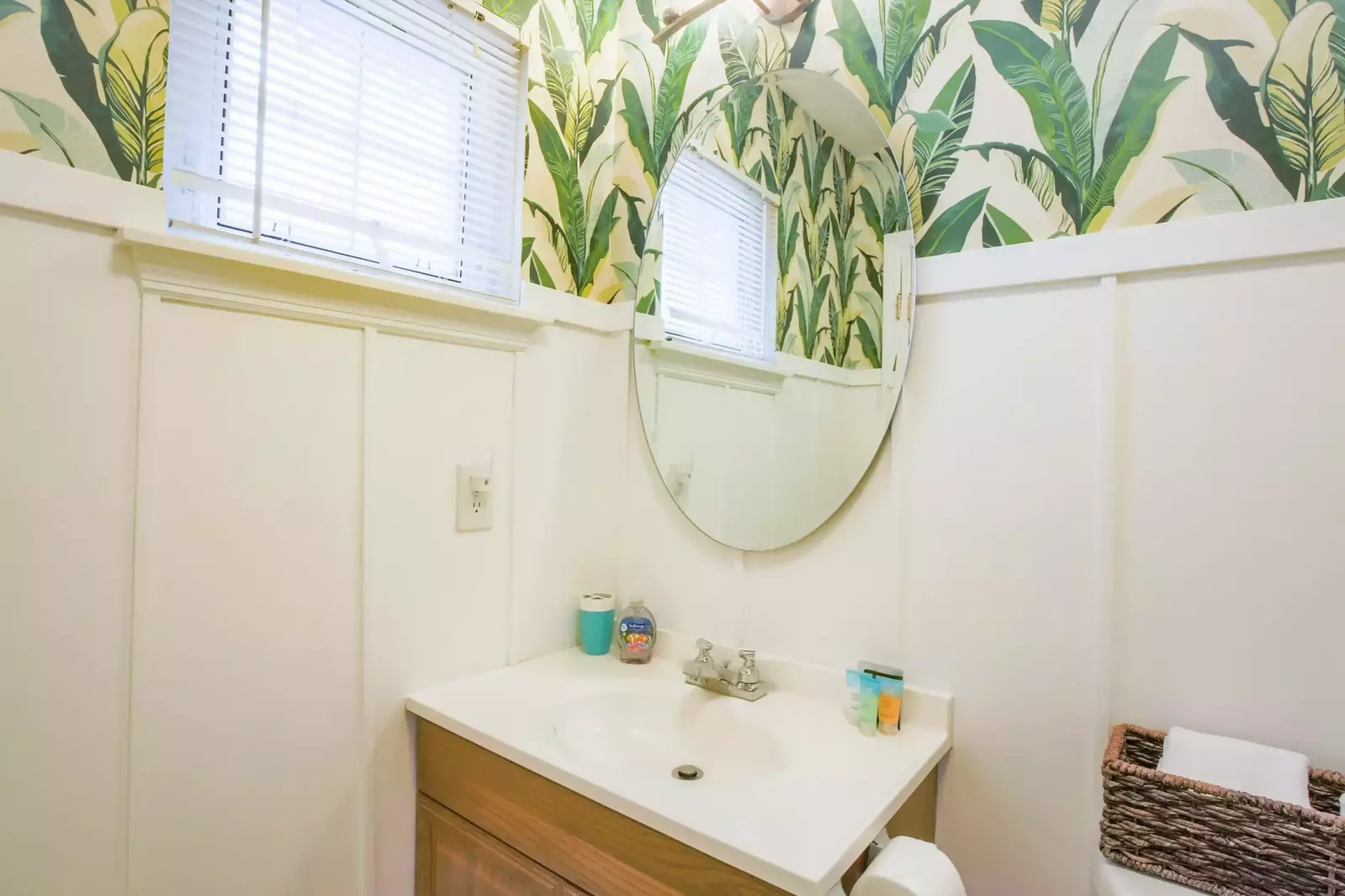 The master bathroom features paneled walls, tropical wallpaper and a vanity.