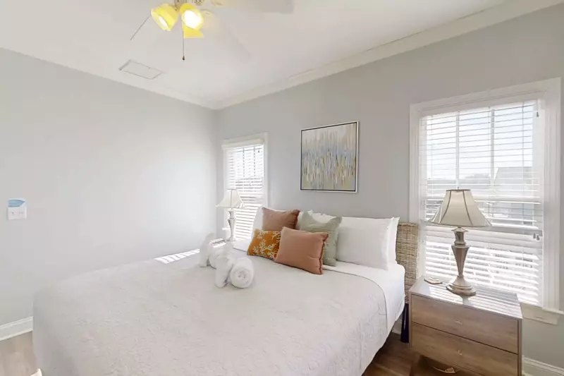 The primary suite features a king bed, night stands with reading lamps and a ceilng fan.