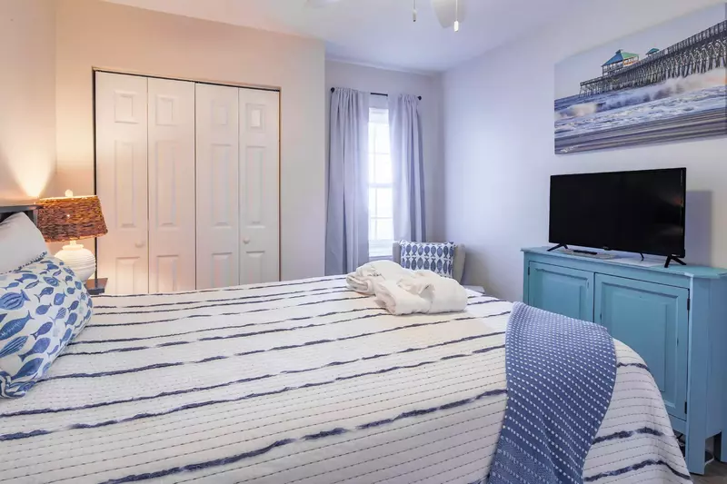 This bedroom has a queen bed, night stand with reading lamp, arm chair and smart TV.