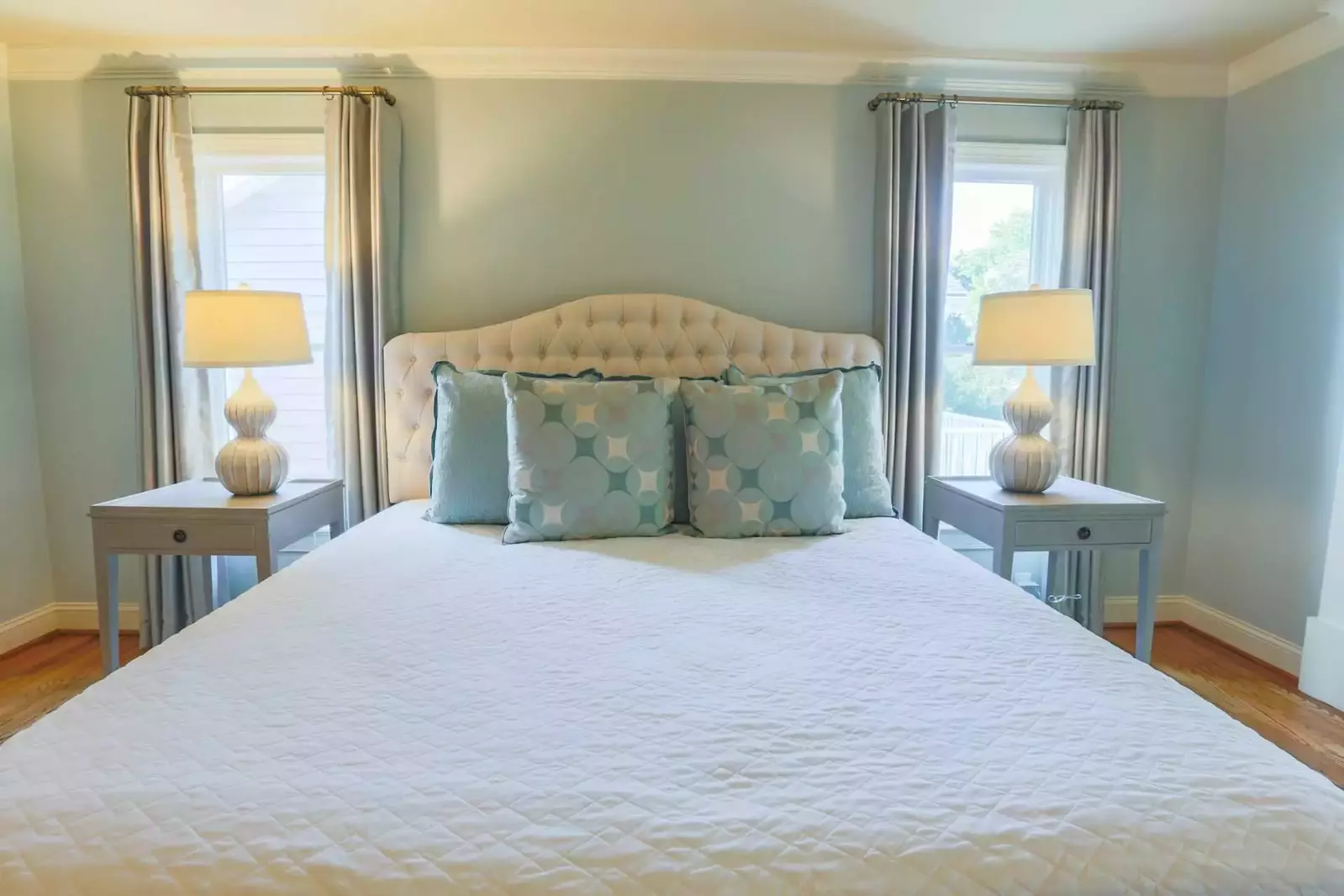 The master suite has a king bed, night stands with reading lamps and curtained windows.