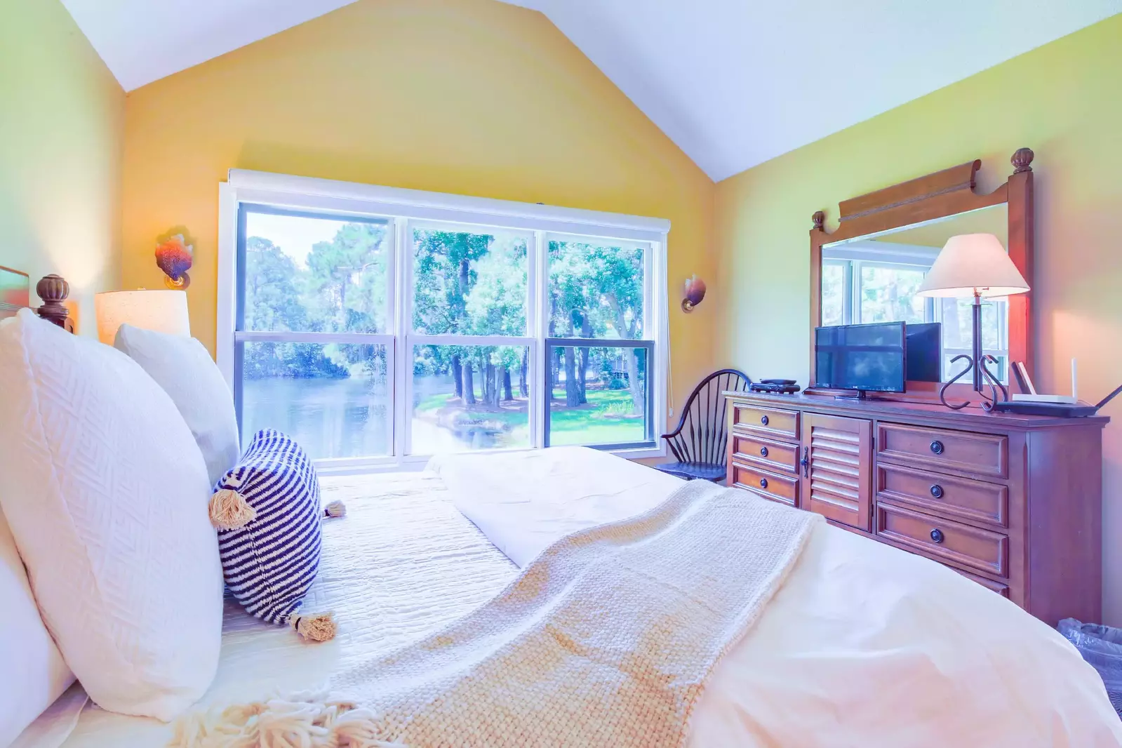The primary suite also has vaulted ceilings, a dresser with TV and a chair.