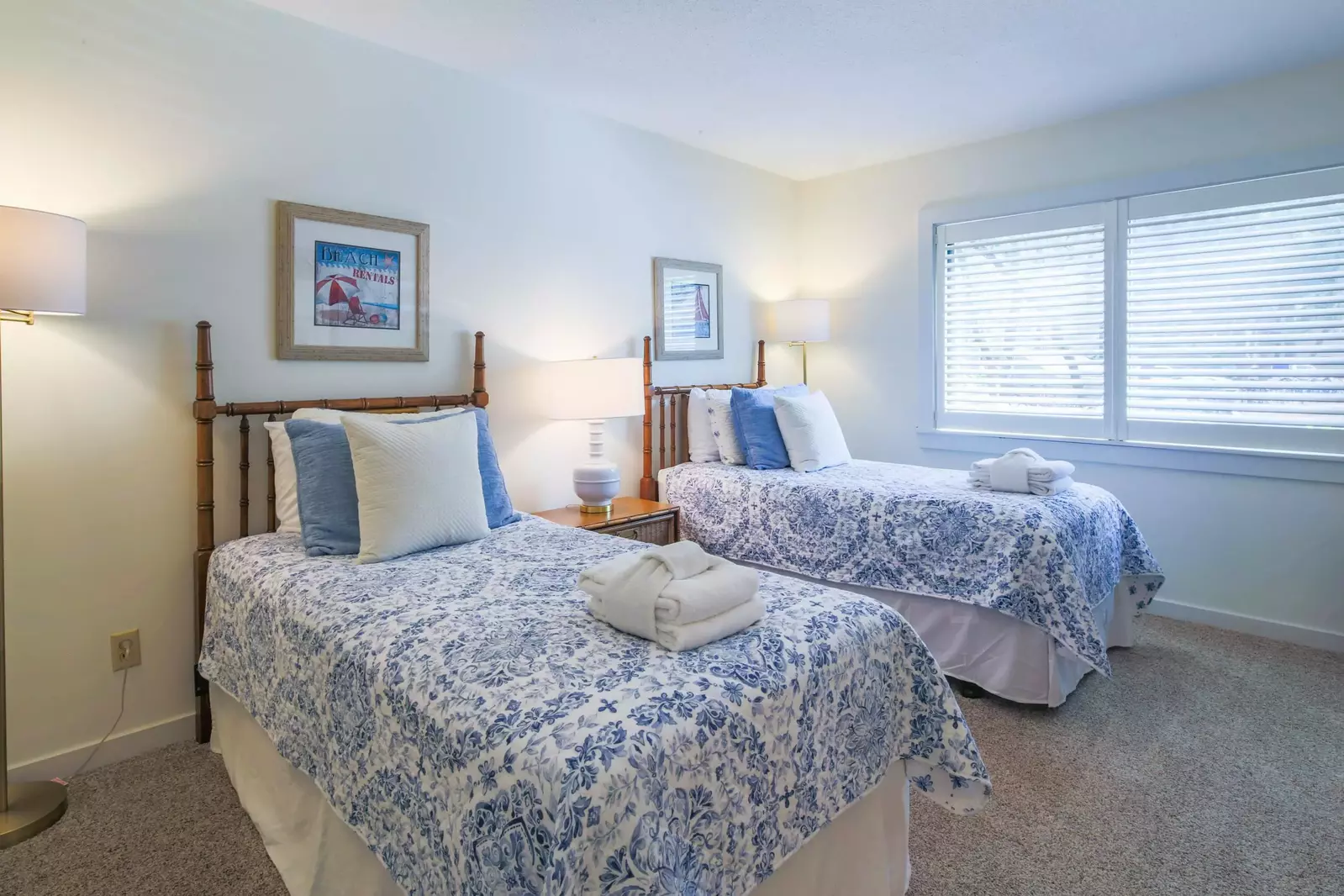 The guest bedroom features two twin beds, a nights stand with a reading lamp and two floor lamps.