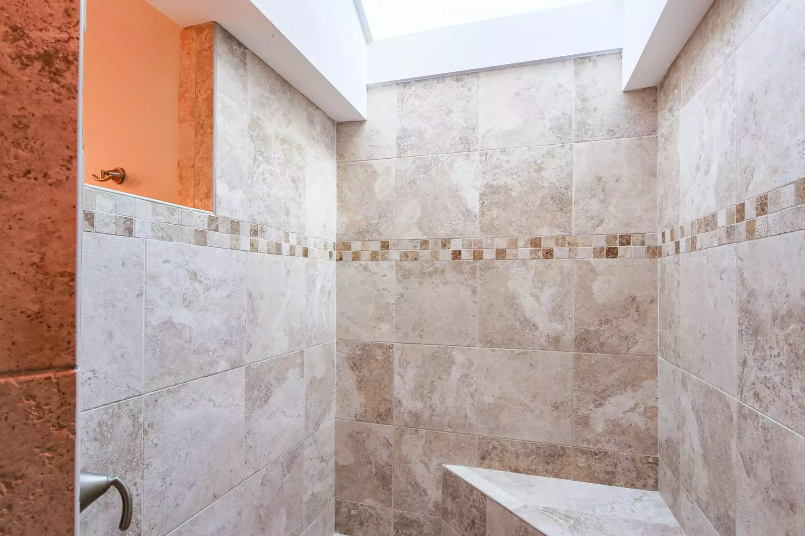 This tiled, walk-in shower features a bench as well as a sky light.