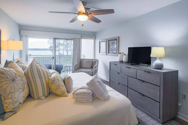 The master suite also features water views, a dresser, TV, arm chair and sliding door access to the balcony.