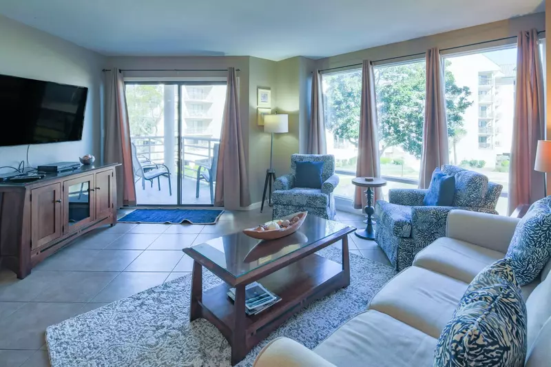 The living room features a spacious seating area, wall-mounted TV and sliding door access to a covered balcony.