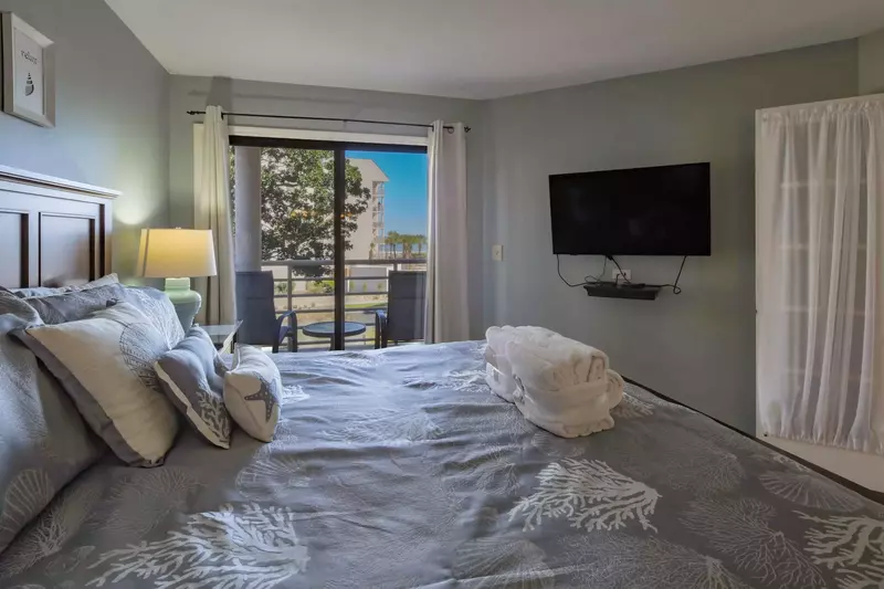 The master suite also has a wall-mounted TV and sliding door access to the covered balcony.