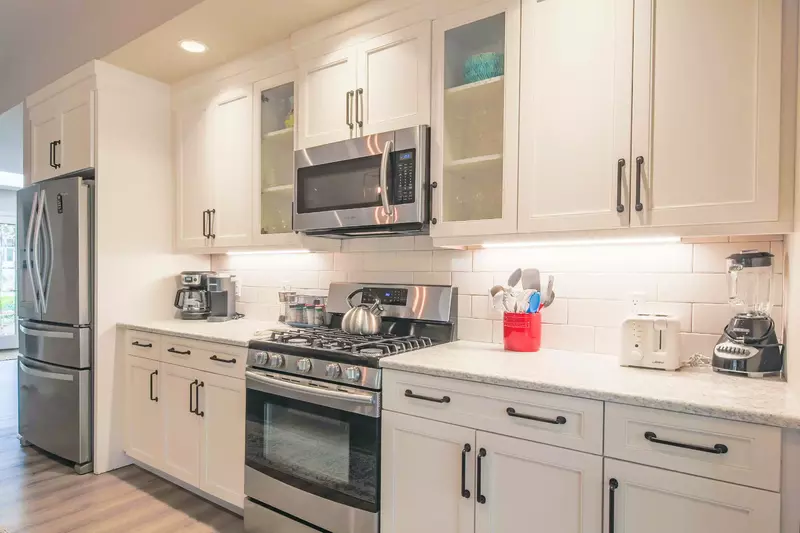 This gorgeous kitchen features white cabinetry, tiled backsplash, undercabinet lighting and stainless steel appliances.