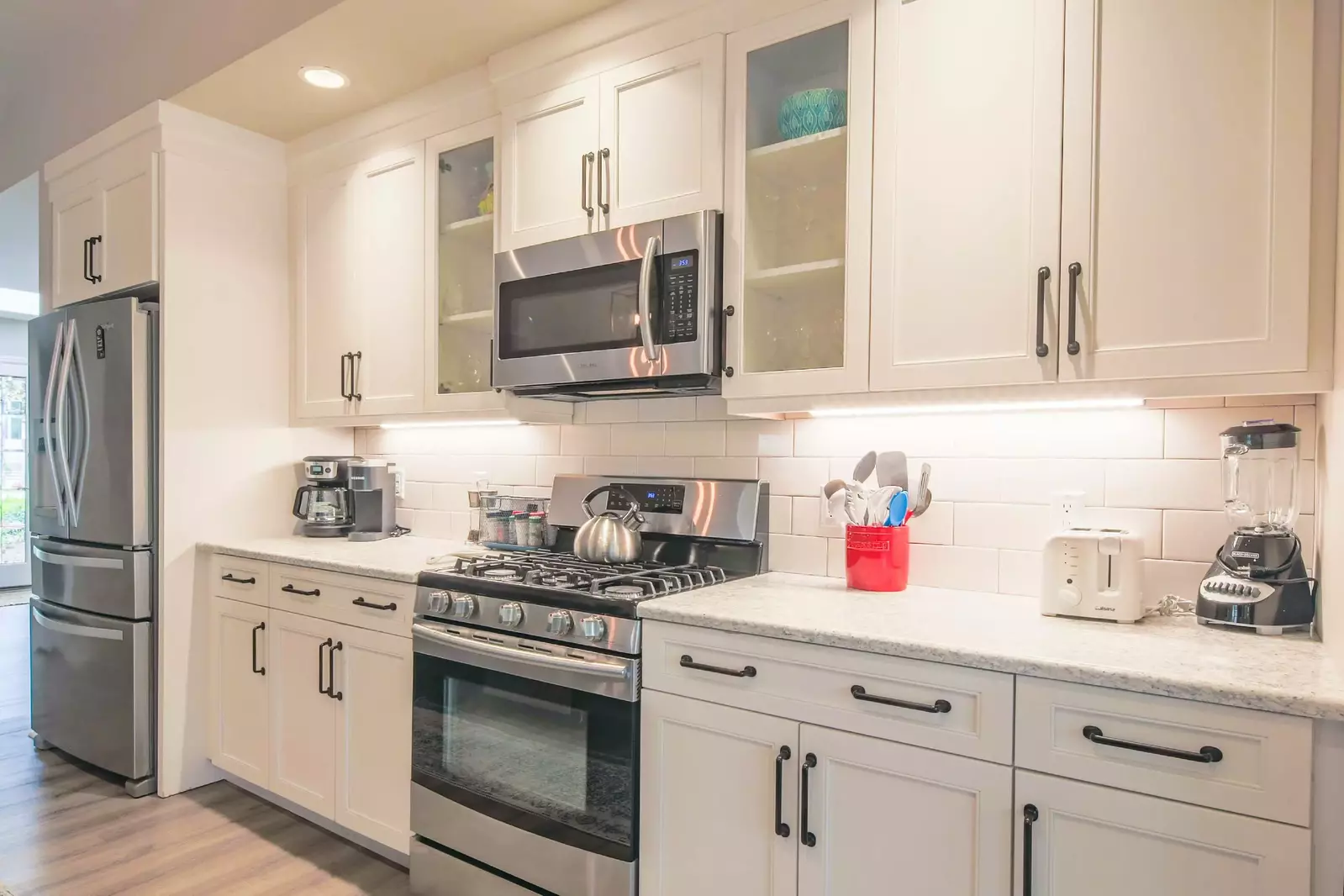 This gorgeous kitchen features white cabinetry, tiled backsplash, undercabinet lighting and stainless steel appliances.