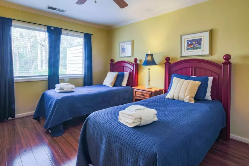 This guest bedroom features two twin beds and a night stand with a reading lamp.