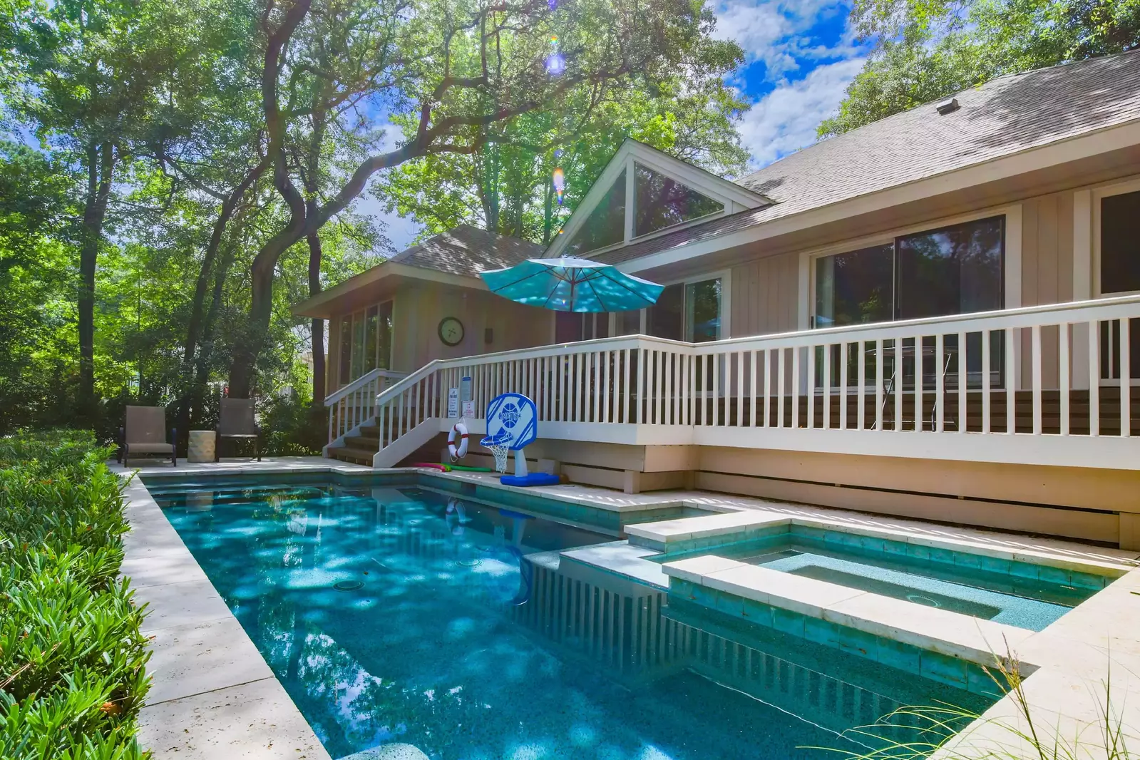 The back deck and pool patio features a outdoor dining table & umbrella, a lounge chair and an outdoor arm chair.
