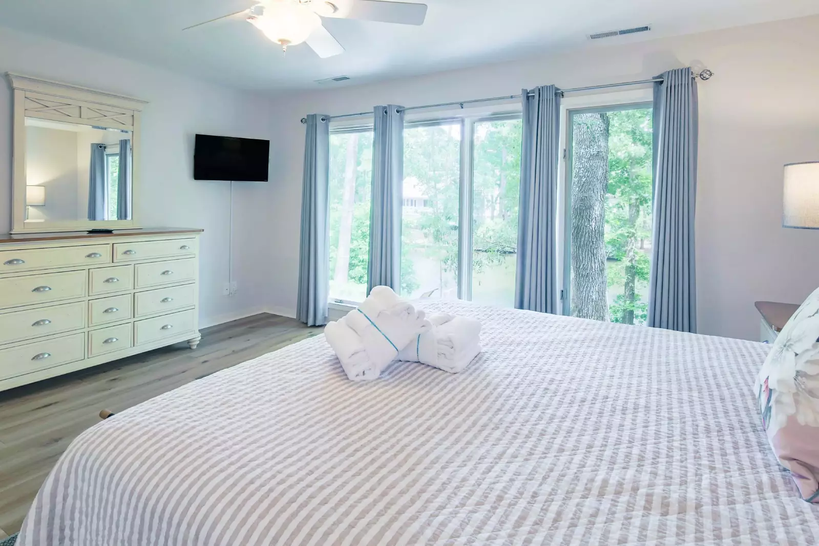 The master suite also features lagoon views, a dresser, ceiling fan and wall-mounted TV.