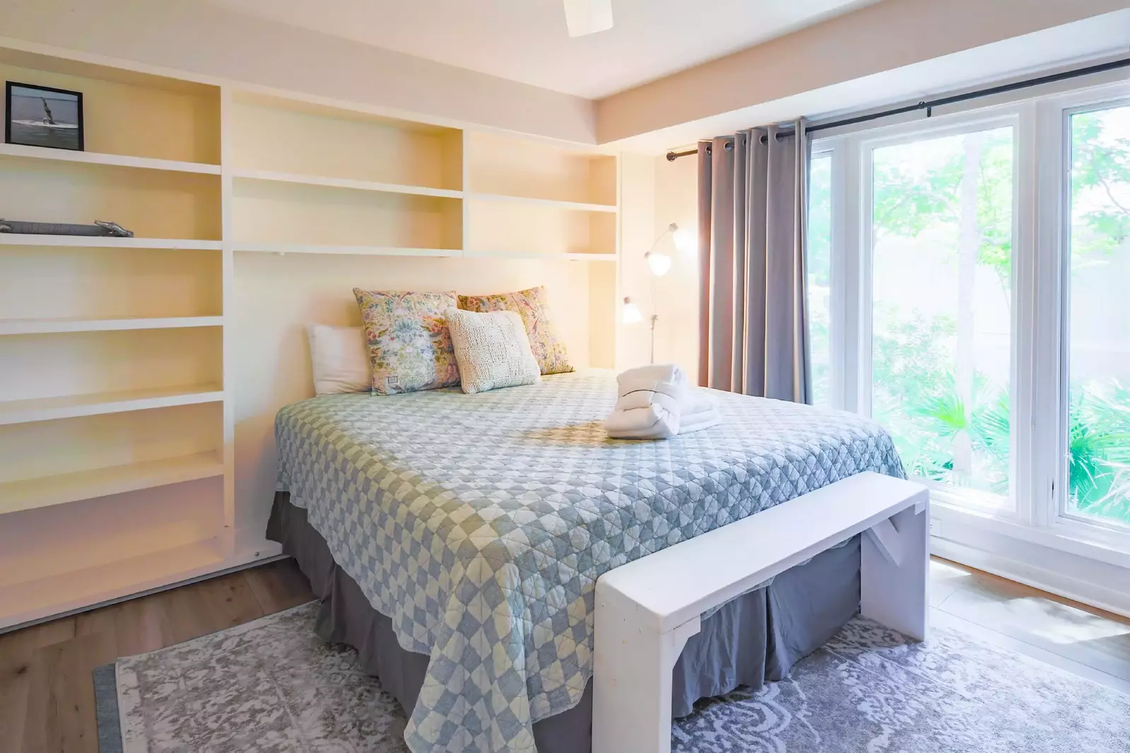 This bedroom features a king bed, bench, floor lamp and large windows.