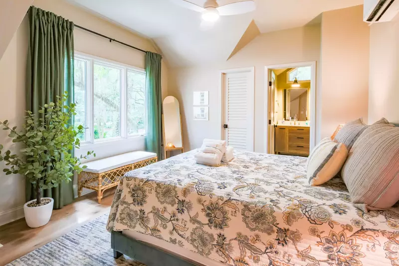 This guest bedroom features a queen bed, bench and large windows.