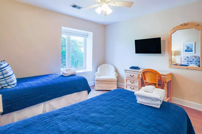 The guest bedroom also features a desk, wall-mounted TV, mirror and ceiling fan.