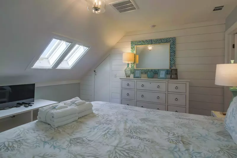 The fifth bedroom features a queen bed, dresser, small TV and sloping ceilings.