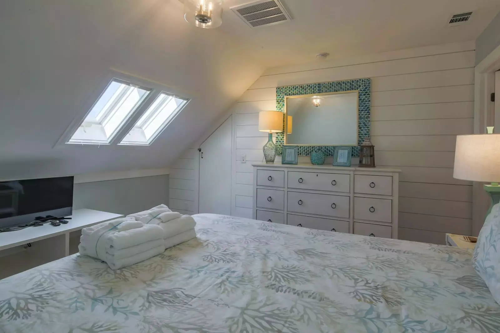 The fifth bedroom features a queen bed, dresser, small TV and sloping ceilings.