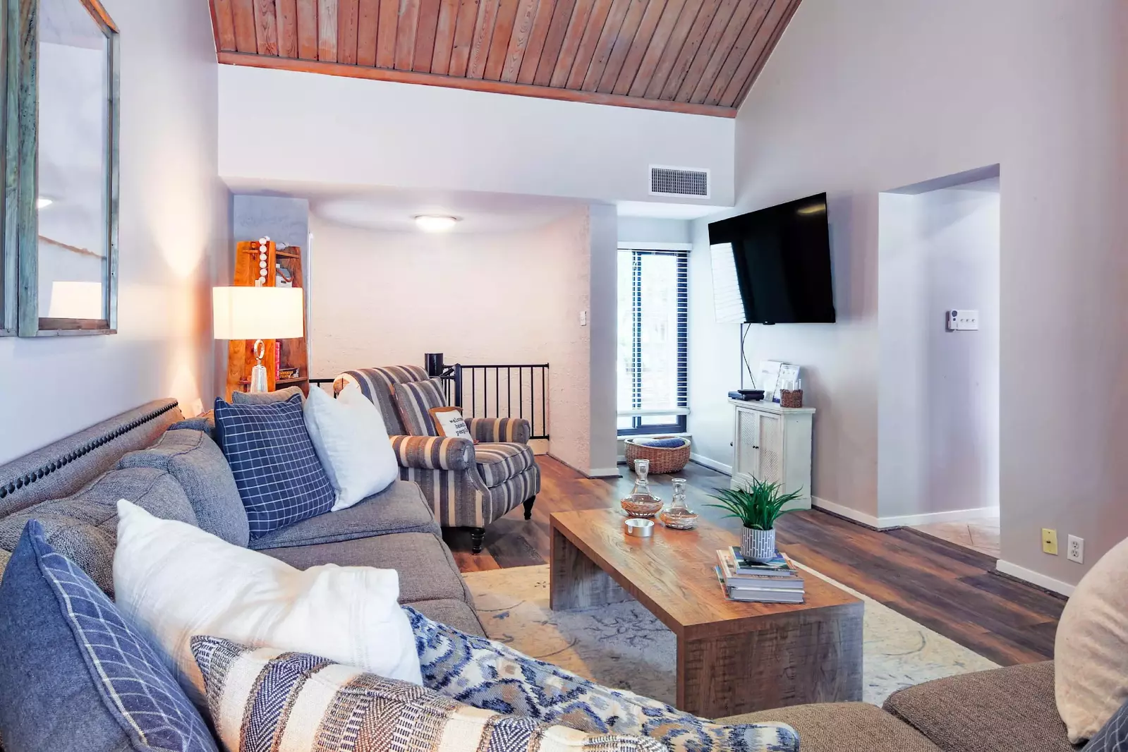 The living room features a spacious sectional, wall-mounted smart TV and vaulted ceilings.