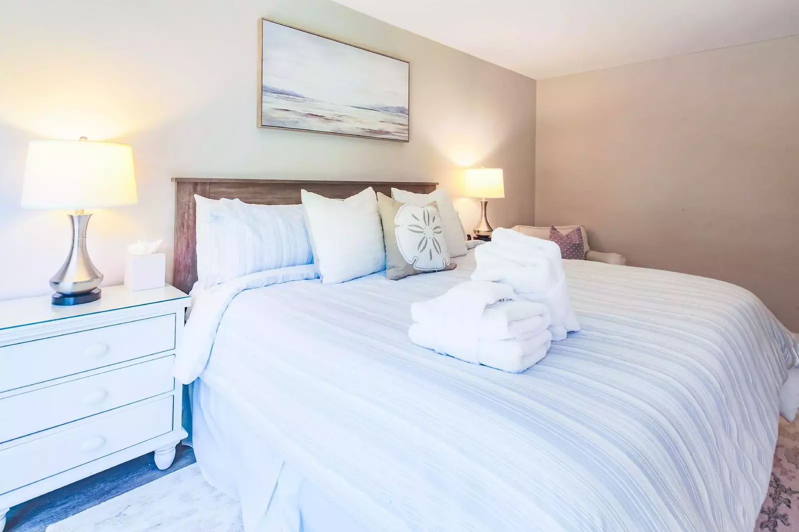The master suite features a king bed, night stands with reading lamps and an arm chair.