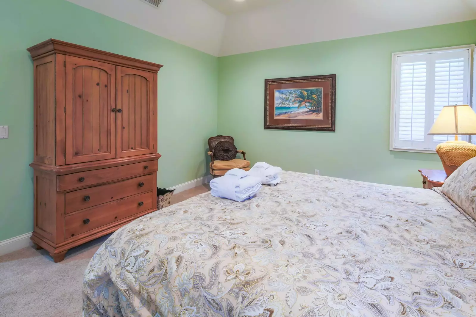 The second master suite features vaulted ceilings, a TV within an armoire and an arm chair.