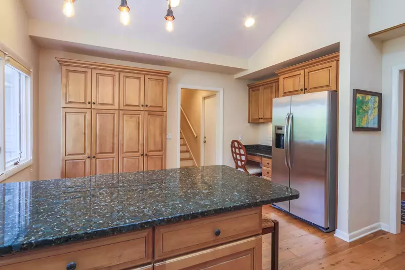 There is a desk in the kitchen near the refrigerator.