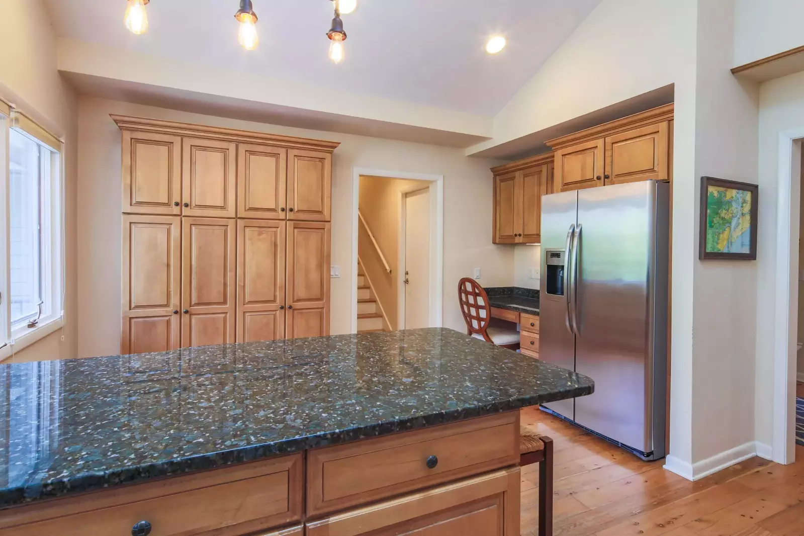 There is a desk in the kitchen near the refrigerator.