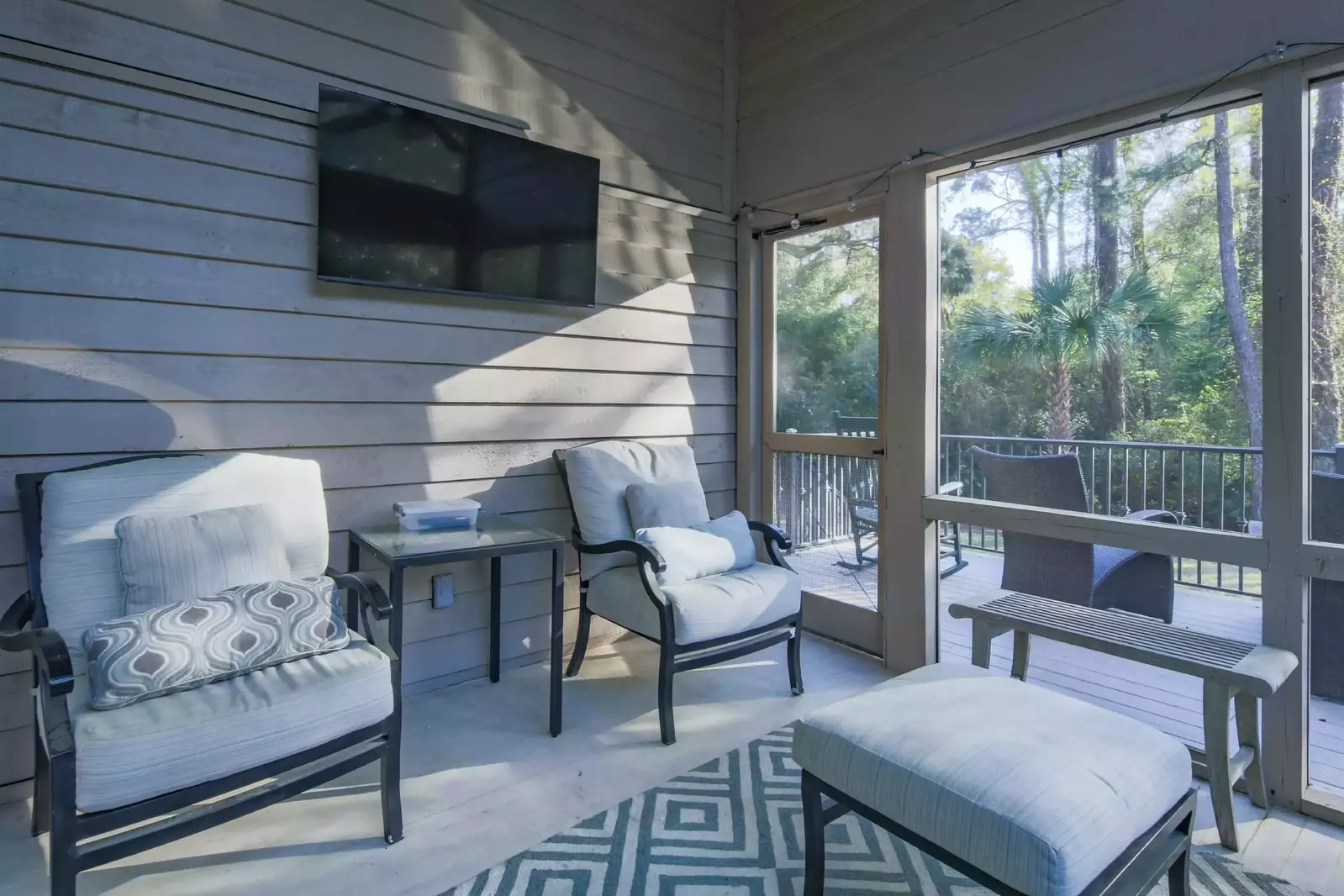 Step out of the dining area and onto the screened porch with a wall-mounted TV and seating area.