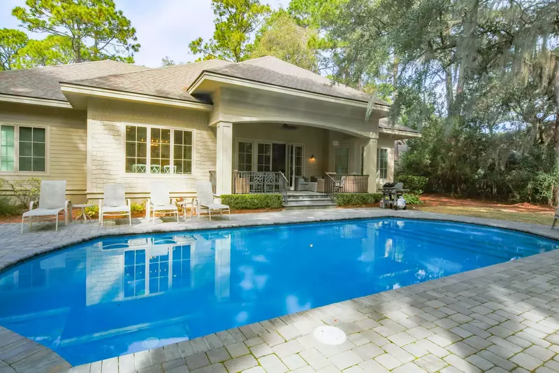 The covered patio steps down to the paved pool area with lounge chairs and a grill.
