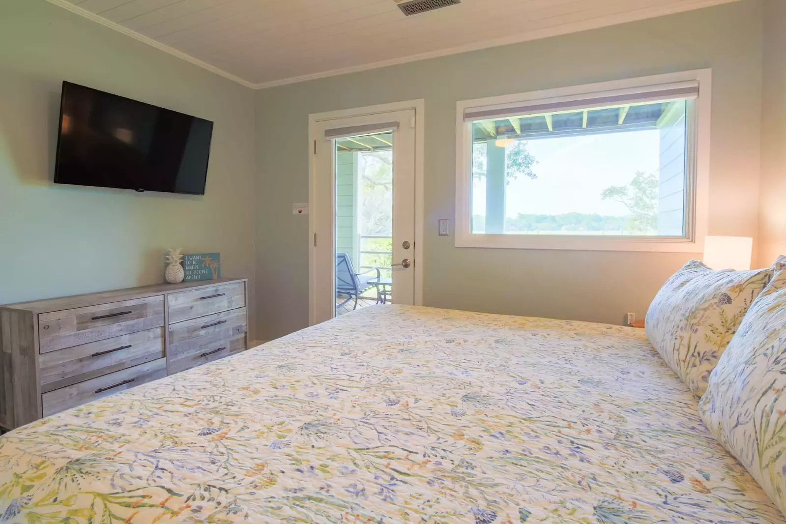 The bedroom features a dresser, wall-mounted TV and access to a covered deck.