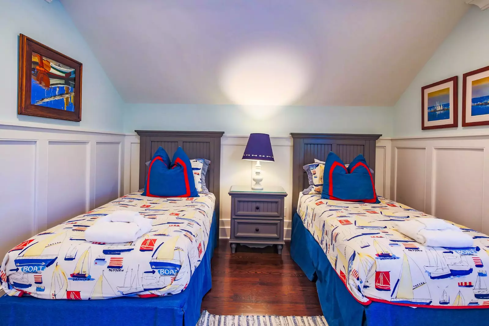This upper level bedroom features two twin beds and a night stand with a reading lamp.