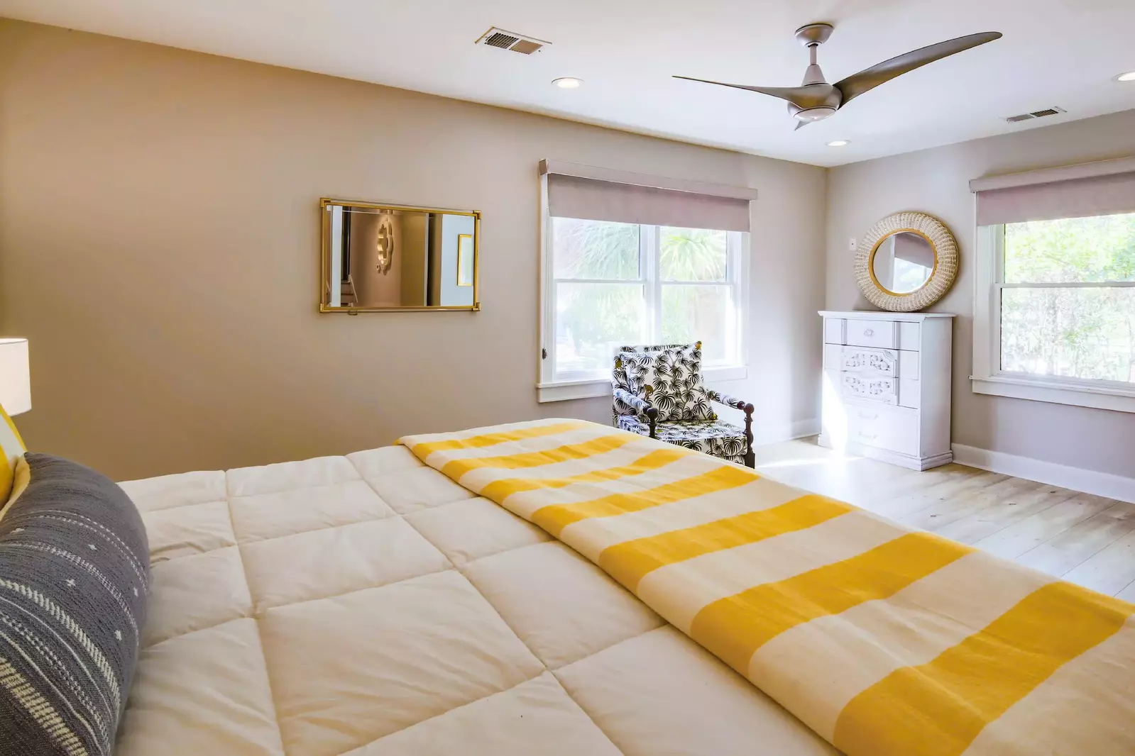 The primary suite also has a ceiling fan, arm chair, dresser and mulitple mirrors.