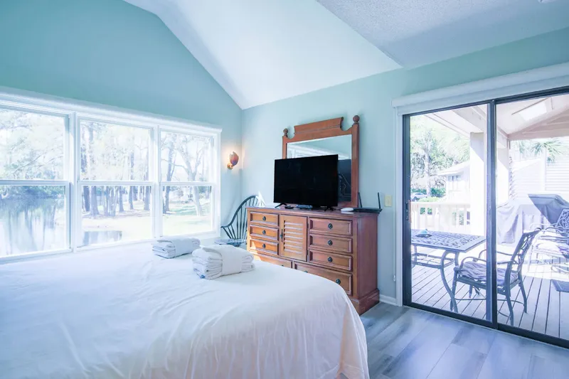 The primary suite features a dresser with TV, a chair and sliding door access to the back deck.