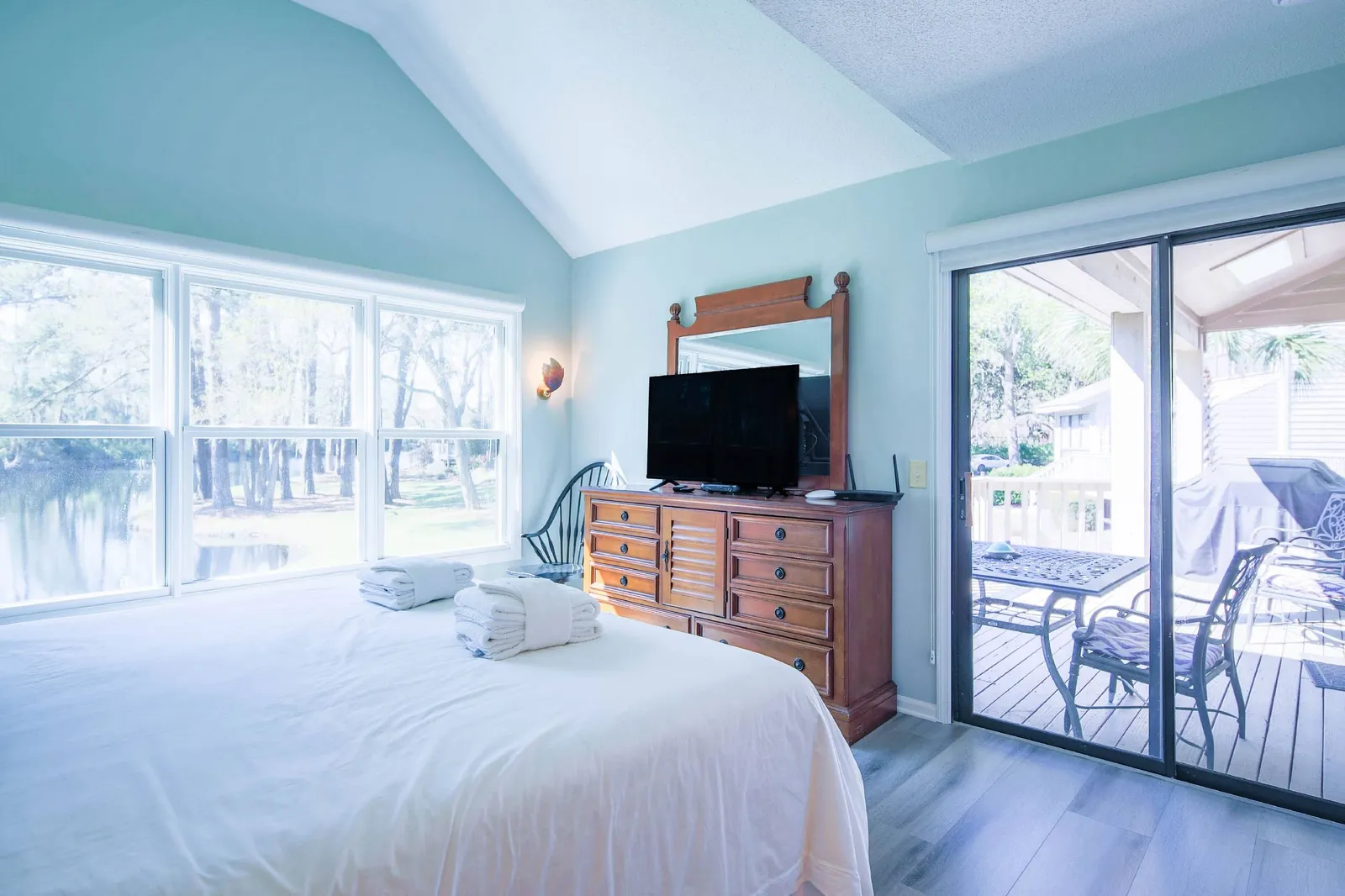 The primary suite features a dresser with TV, a chair and sliding door access to the back deck.