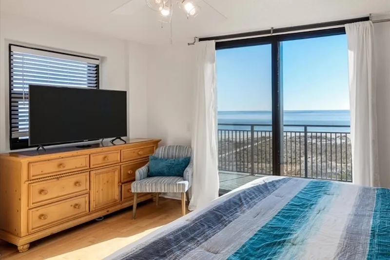 The primary suite also features a dresser, smart TV, arm chair and ocean views.