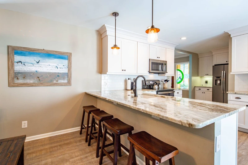 The beautiful kitchen features granite counters, white cabinets, stainless steel appliances and 4 stools.