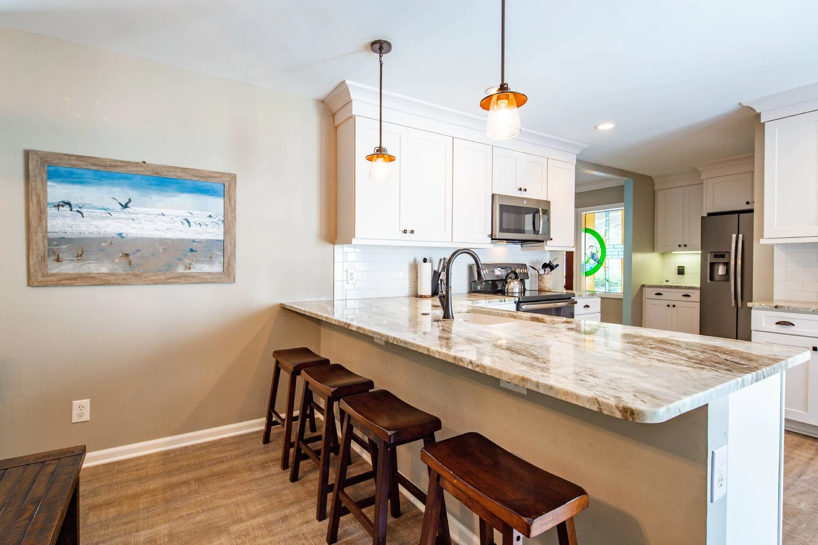 The beautiful kitchen features granite counters, white cabinets, stainless steel appliances and 4 stools.