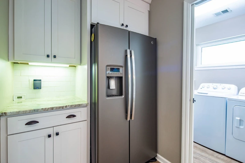 The laundry room is located near the refrigerator in the kitchen.
