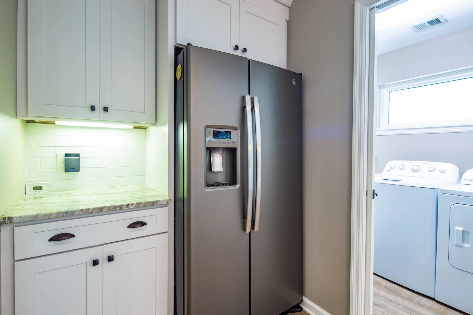 The laundry room is located near the refrigerator in the kitchen.