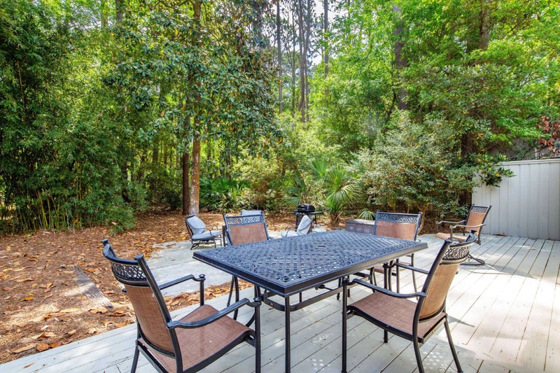 The back deck features an outdoor dining table & chairs and a natural privacy fence of Lowcountry shrubs & trees.