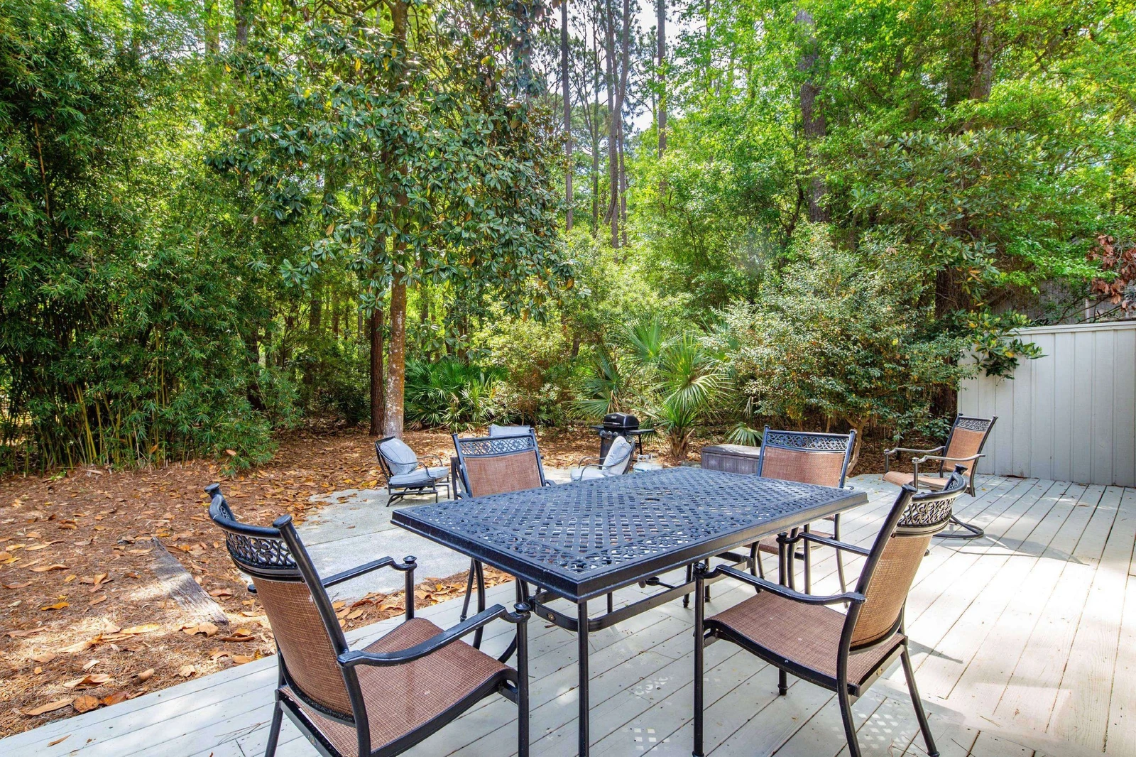 The back deck features an outdoor dining table & chairs and a natural privacy fence of Lowcountry shrubs & trees.