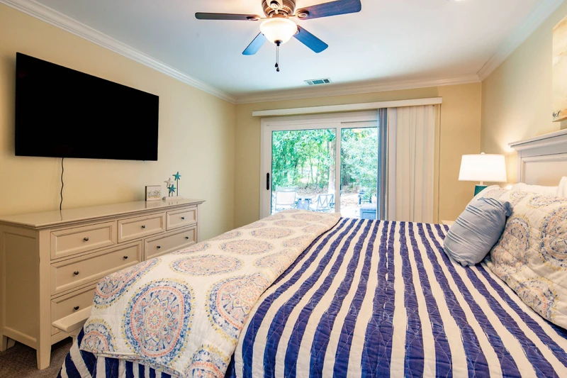 The primary suite also features a dresser, wall-mounted smart TV, ceiling fan and access to the back deck.