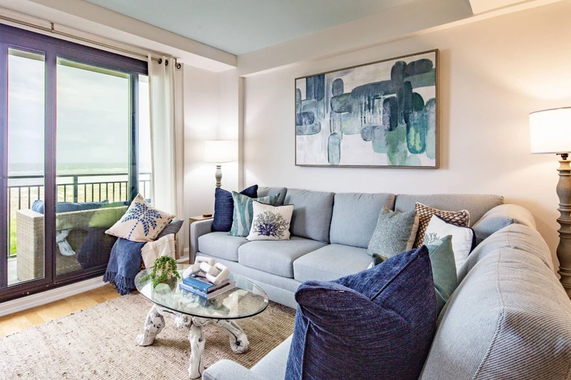 The living room features a spacious seating area, access to a balcony and ocean views.